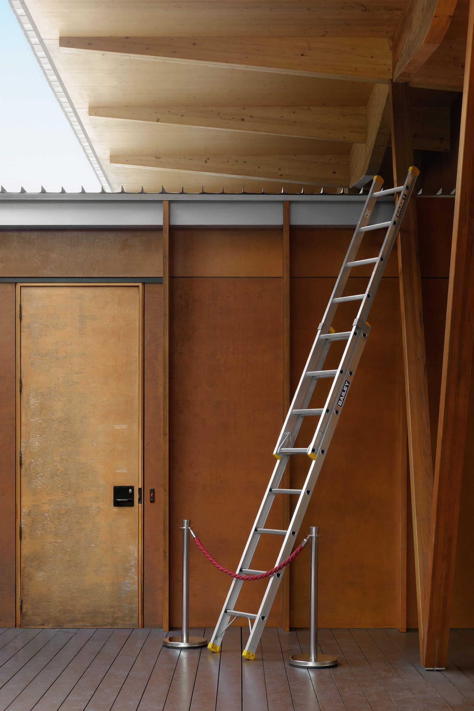 Red braided rope pressed against heavy-duty aluminium extension ladder against a wooden building